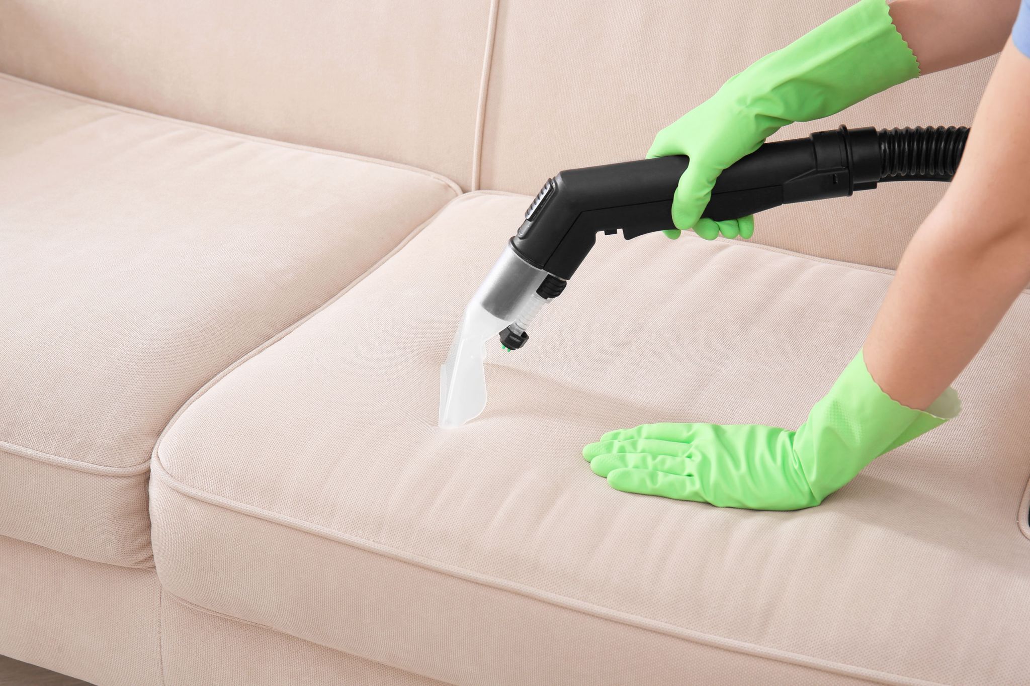 Woman cleaning couch with vacuum cleaner at home